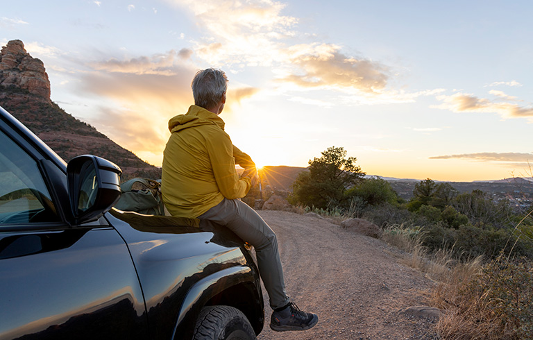 Mature man sitting on the hood of his car looking at the sunset