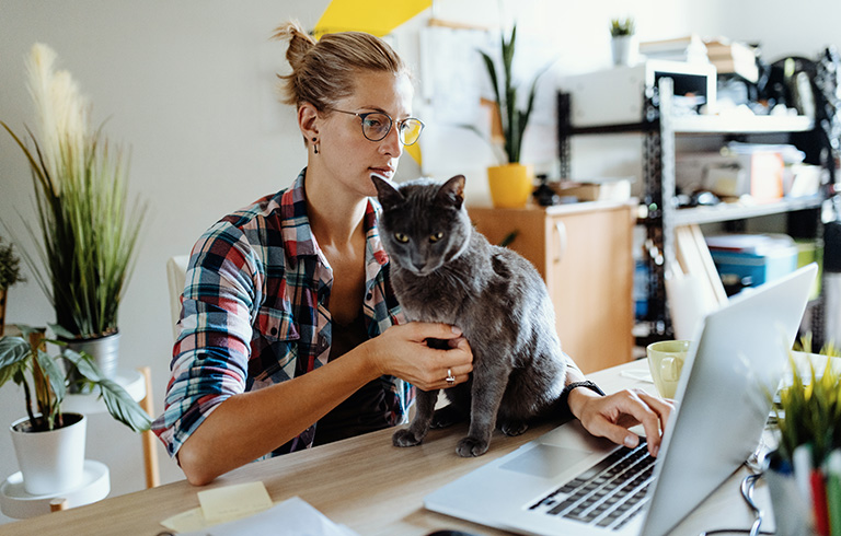 Woman working on her laptop with her cat in front of her