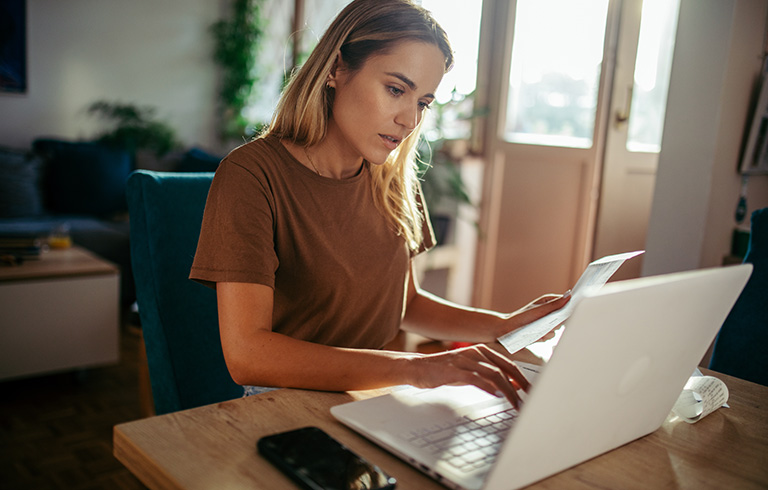 woman working at her laptop while looking at a paper