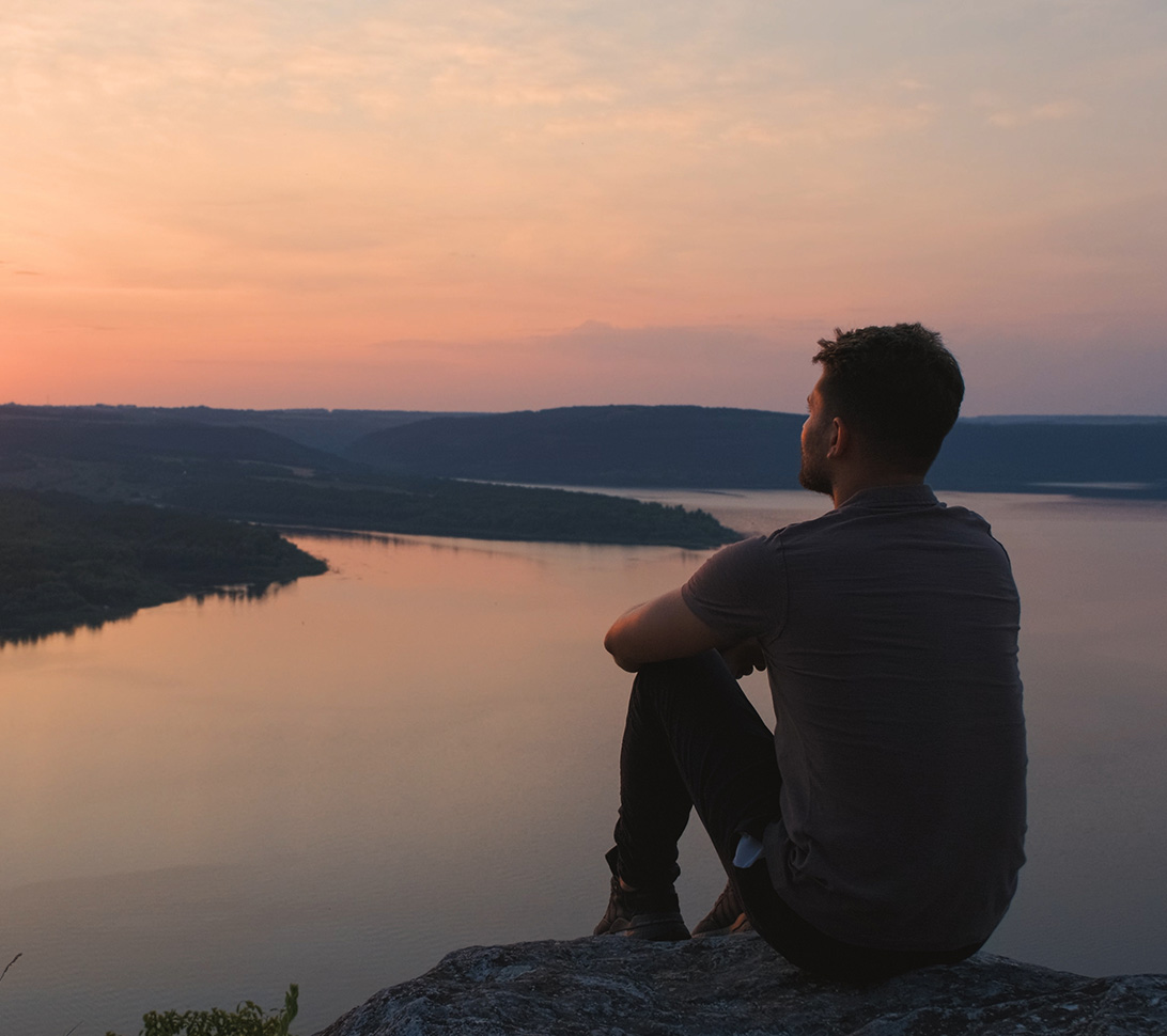 boy sitting on the ground looking out at the sunset