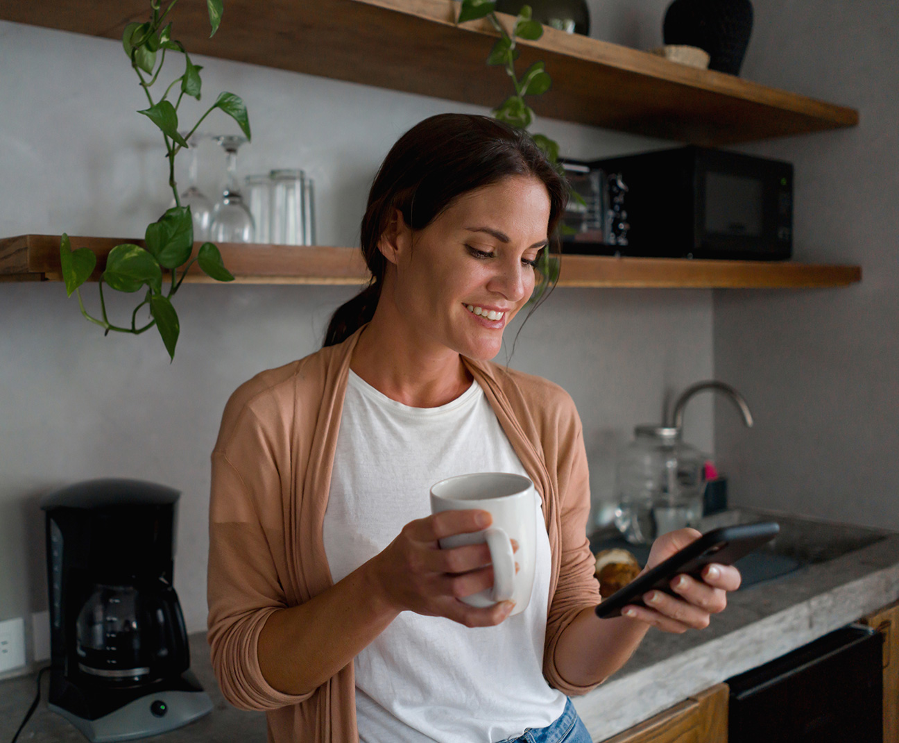 woman drinking coffee in the kitchen while on her phone