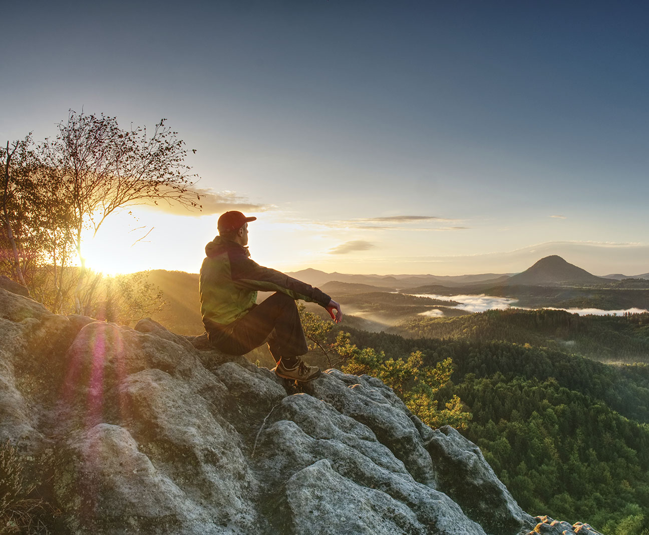 man sitting on a cliff looking out at mountain scenery