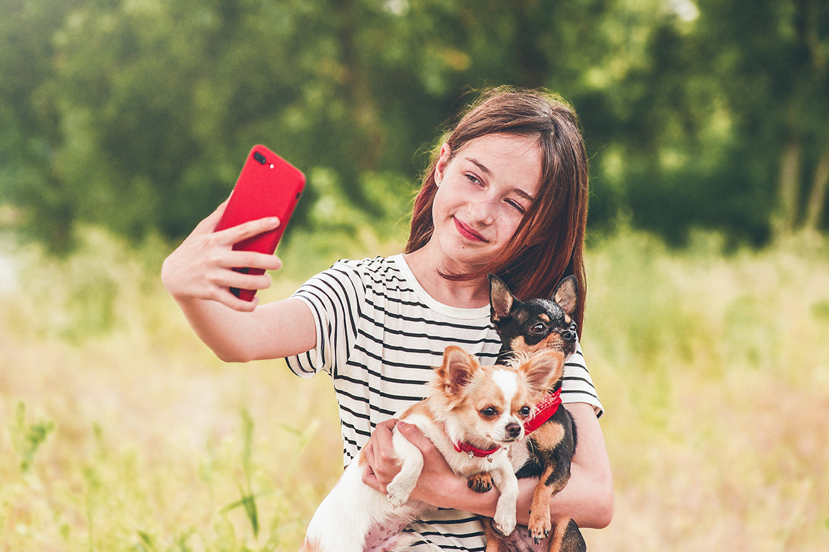 little girl taking a selfie while holding two small dogs