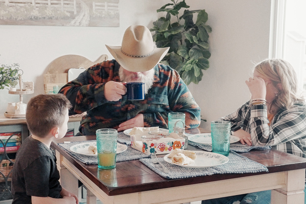 man with cowboy hat sipping coffee at breakfast table with two children