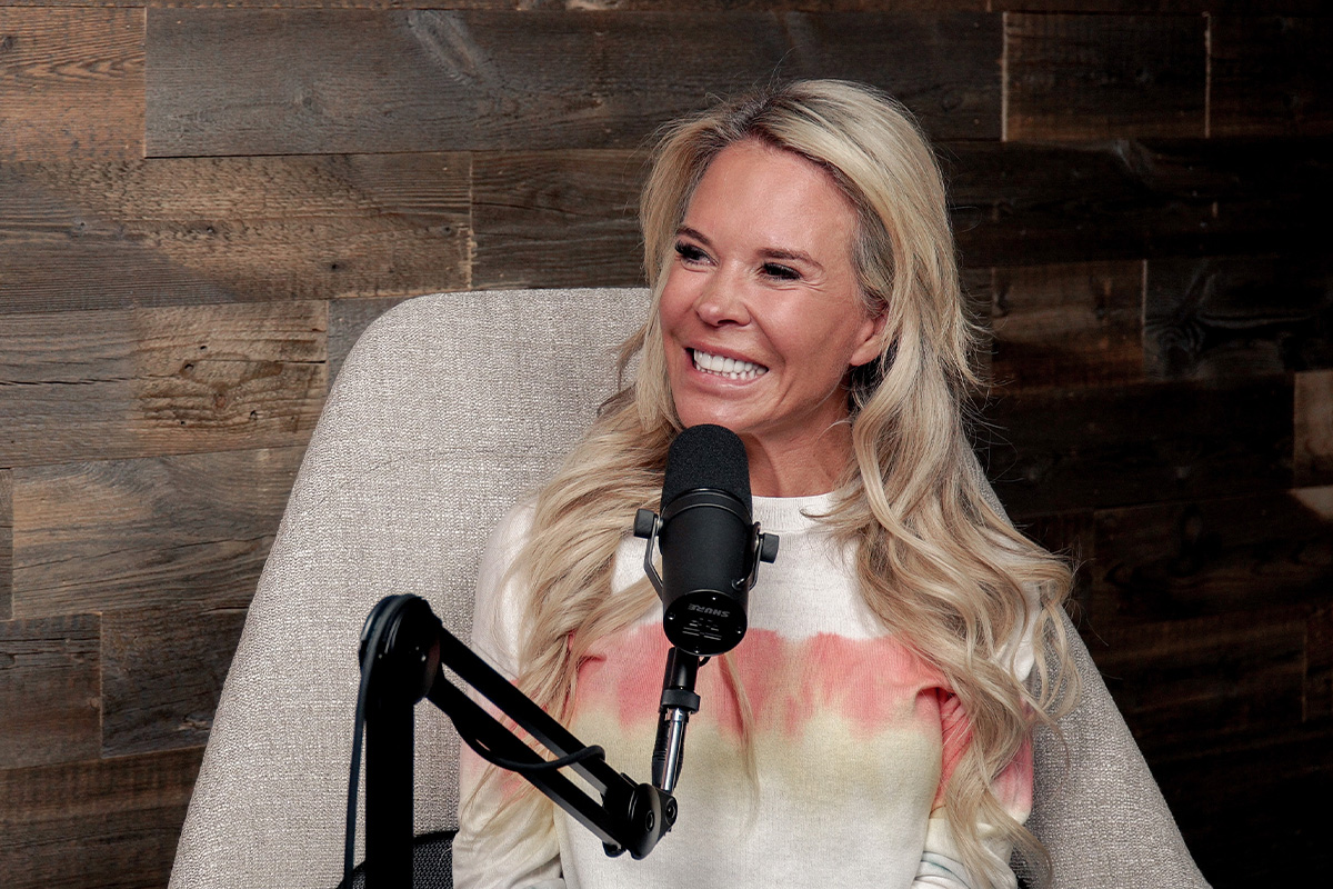 woman with long blonde hair and big smile at podcast mic