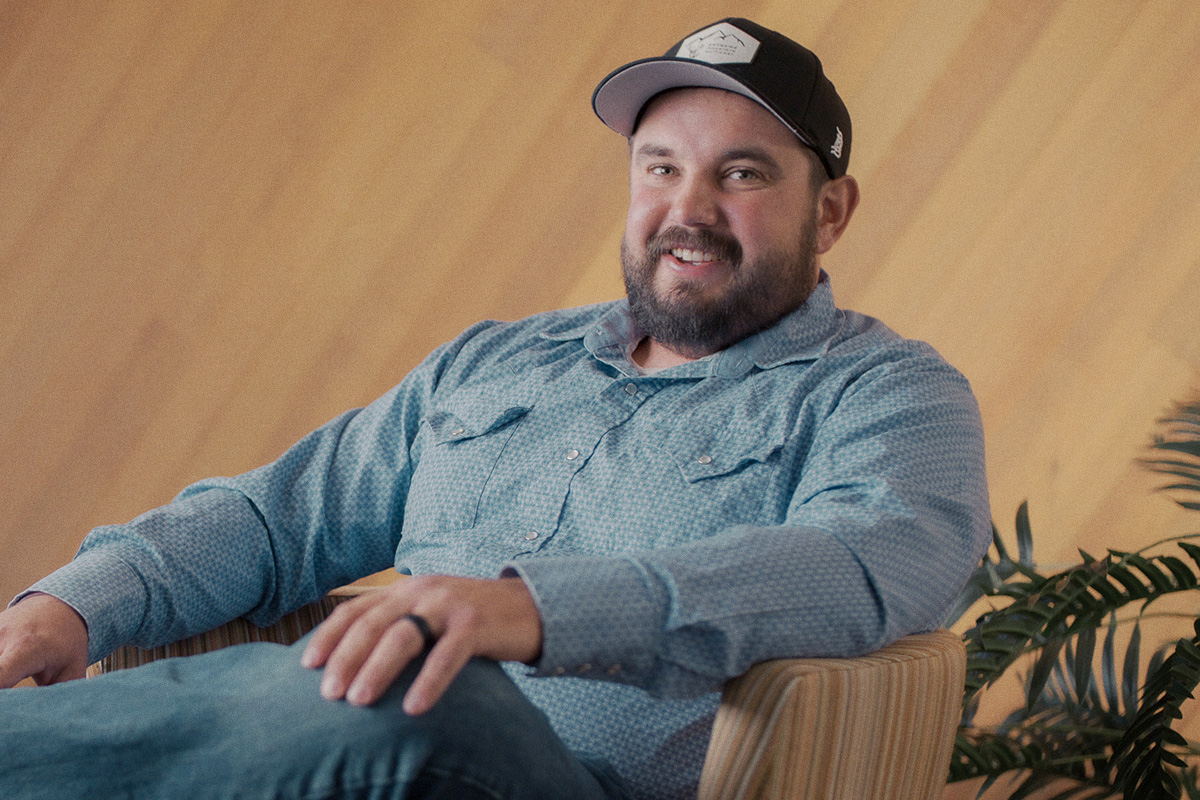 man with beard and ball cap sitting in chair smiling