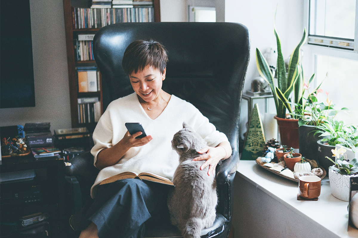 woman sitting on chair looking at mobile phone with cat