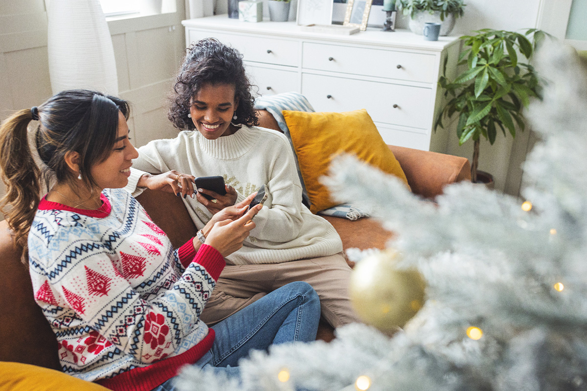 Two women sitting on couch smiling and looking at phones