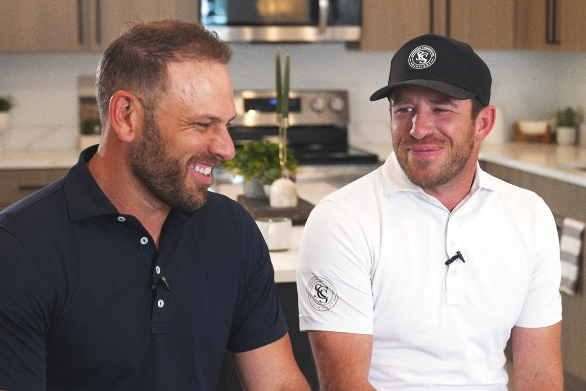 two men in golf shirts sitting in a kitchen laughing with each other