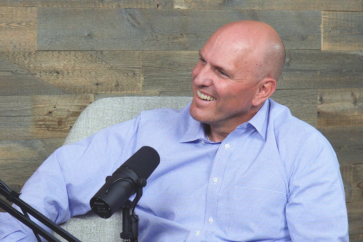 smiling bald man in blue shirt at podcast mic