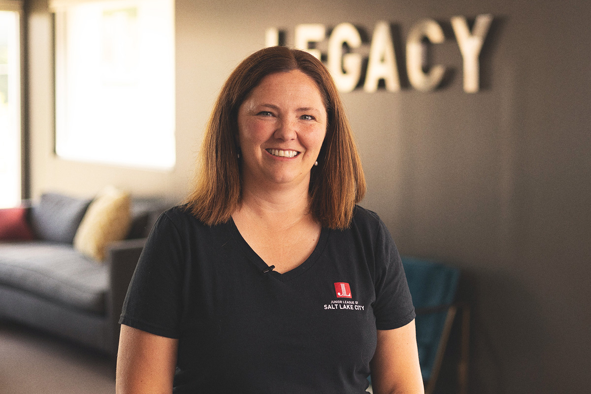 woman sitting in front of grey wall that says "legacy" and smiling at the camera