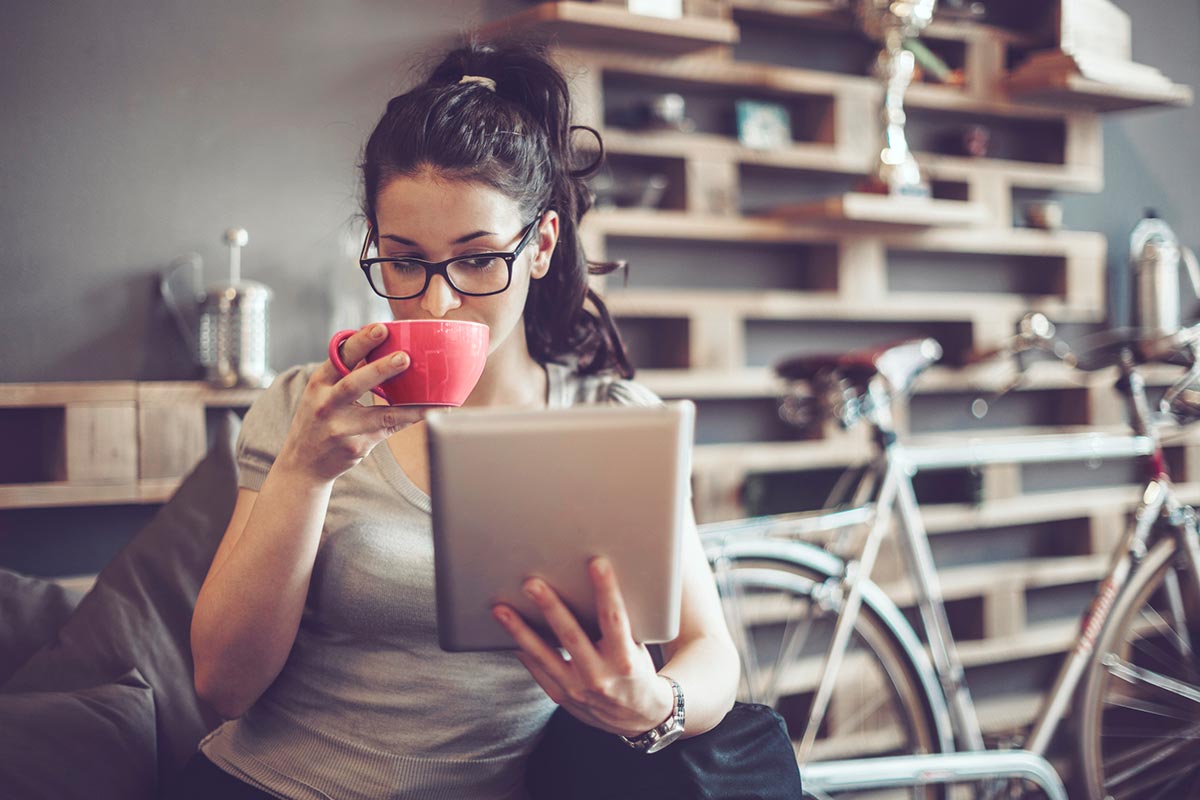 woman sipping out of a mug looking at her tablet