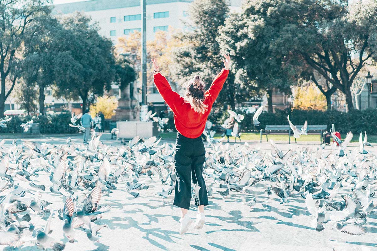 young woman jumping in a swarm of pigeons