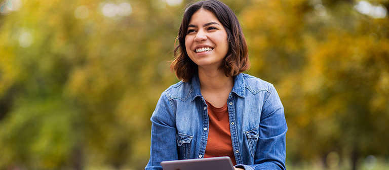 female student smiling outside while using a tablet