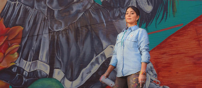 Artist La Morena standing in front of her mural