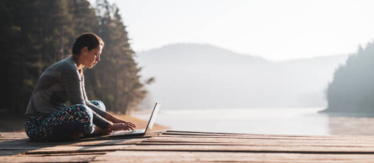 Woman using laptop outdoor at wooden pier.